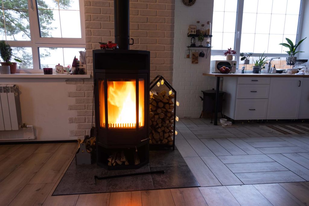Black metal stove fireplace with wood in a woodpile - the interior of a private village house. Heating and heating of the house with firewood, the heat of the fire from the hearth.